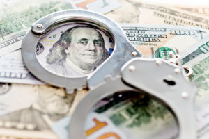 Handcuffs laying on top on American money symbolizing money laundering in West Palm Beach.